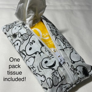 Op de afbeelding: Een witte tissuehouder met rits met een zwart-witte Peanuts-print. De houder is open en er is een witte tissue uitgetrokken. Een pak tissues is inbegrepen.