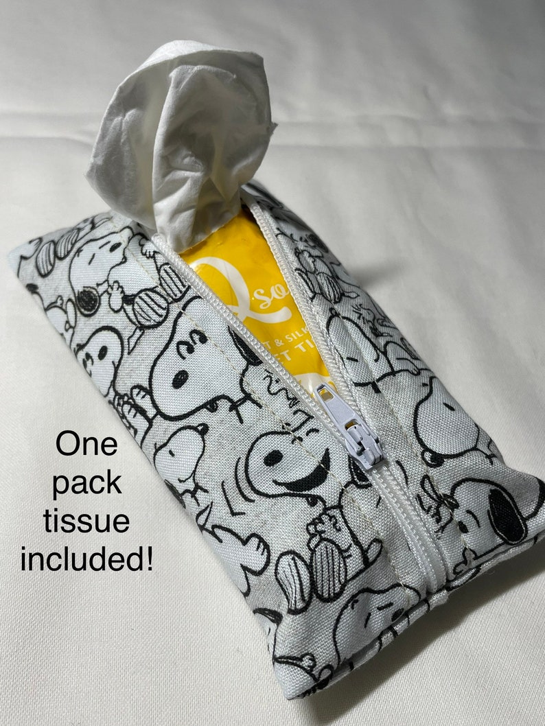 Op de afbeelding: Een witte tissuehouder met rits met een zwart-witte Peanuts-print. De houder is open en er is een witte tissue uitgetrokken. Een pak tissues is inbegrepen.