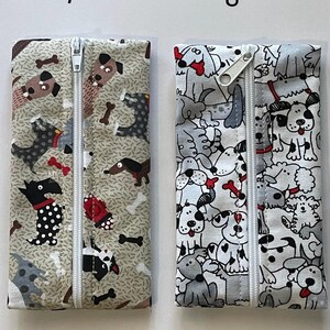 May include: Two rectangular fabric pouches with centre zippers. Pouch 7 features a tan background with various dog breeds and bones. Pouch 8 features a white background with a dense pattern of black, grey, and white cartoon dogs and red bones.