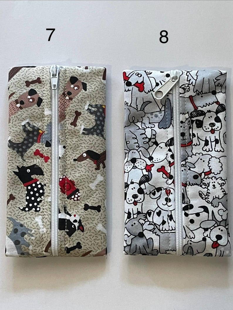 May include: Two rectangular fabric pouches with centre zippers. Pouch 7 features a tan background with various dog breeds and bones. Pouch 8 features a white background with a dense pattern of black, grey, and white cartoon dogs and red bones.