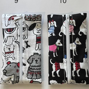 May include: Two rectangular fabric pouches with centre zippers. The left pouch is white with a black and red dog print. The right pouch is black with a colourful dog print featuring various outfits. Both pouches are labelled with the numbers 9 and 10.
