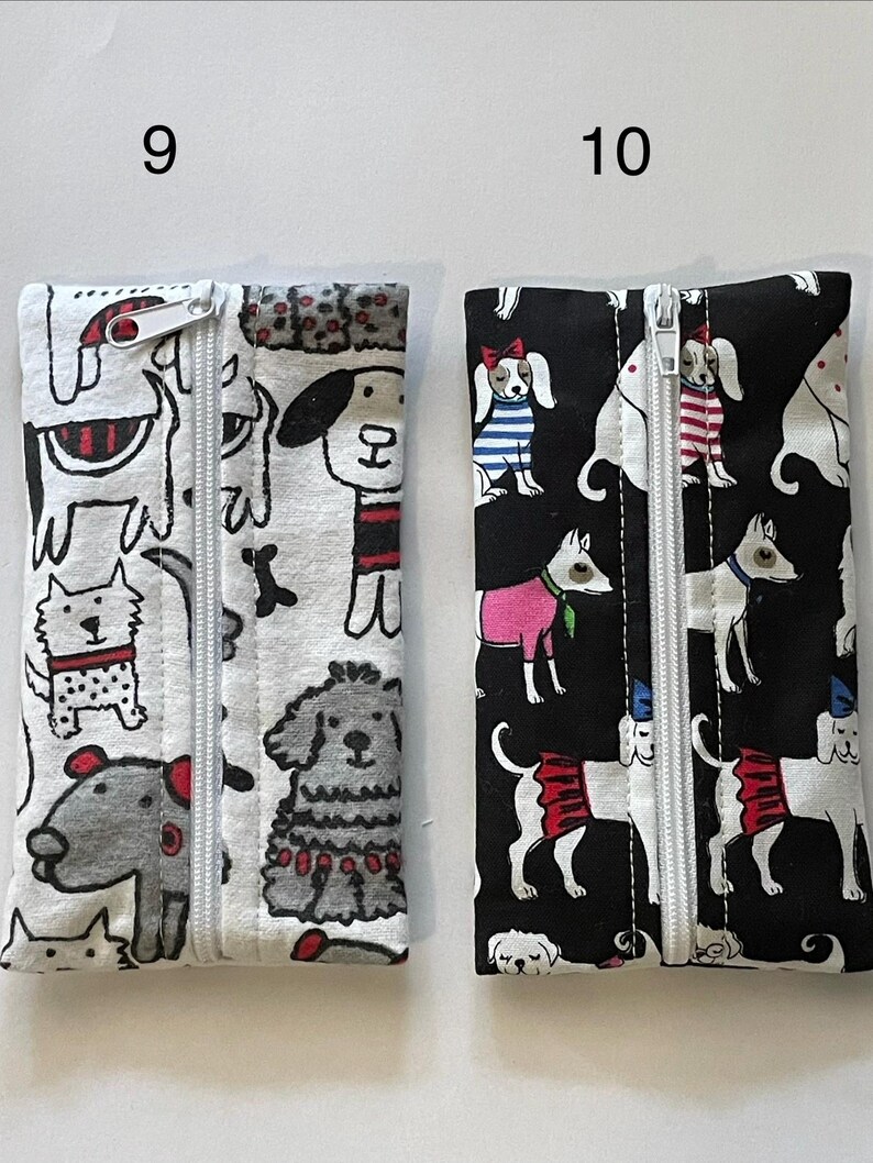 May include: Two rectangular fabric pouches with centre zippers. The left pouch is white with a black and red dog print. The right pouch is black with a colourful dog print featuring various outfits. Both pouches are labelled with the numbers 9 and 10.
