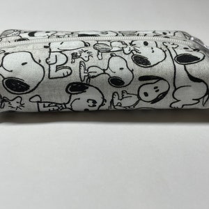 Op de afbeelding: Een wit canvas potlood etui met een zwart-witte print van Snoopy en Woodstock.