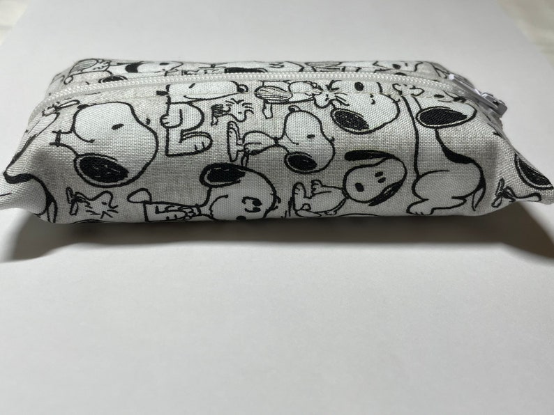 Op de afbeelding: Een wit canvas potlood etui met een zwart-witte print van Snoopy en Woodstock.