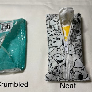 Op de afbeelding: Twee tissueboxen, een gekreukeld en een netjes. De nette doos is wit met een zwart-wit patroon van Snoopy-figuren. De doos heeft een ritssluiting.