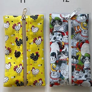 May include: Two rectangular fabric pouches with centre zippers. Pouch 11 is yellow with a black and white chicken pattern. Pouch 12 features a multi-coloured cat print with various feline faces. Both items are labelled with the numbers 11 and 12.