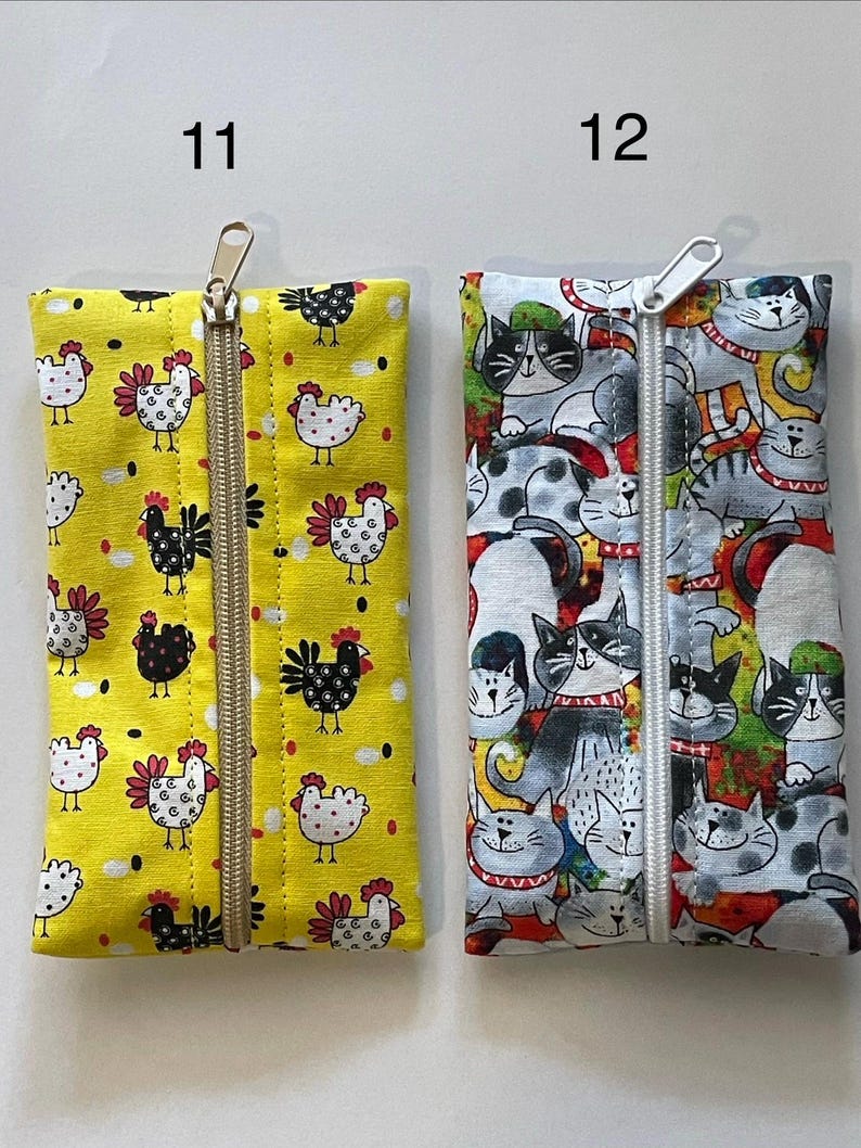 May include: Two rectangular fabric pouches with centre zippers. Pouch 11 is yellow with a black and white chicken pattern. Pouch 12 features a multi-coloured cat print with various feline faces. Both items are labelled with the numbers 11 and 12.