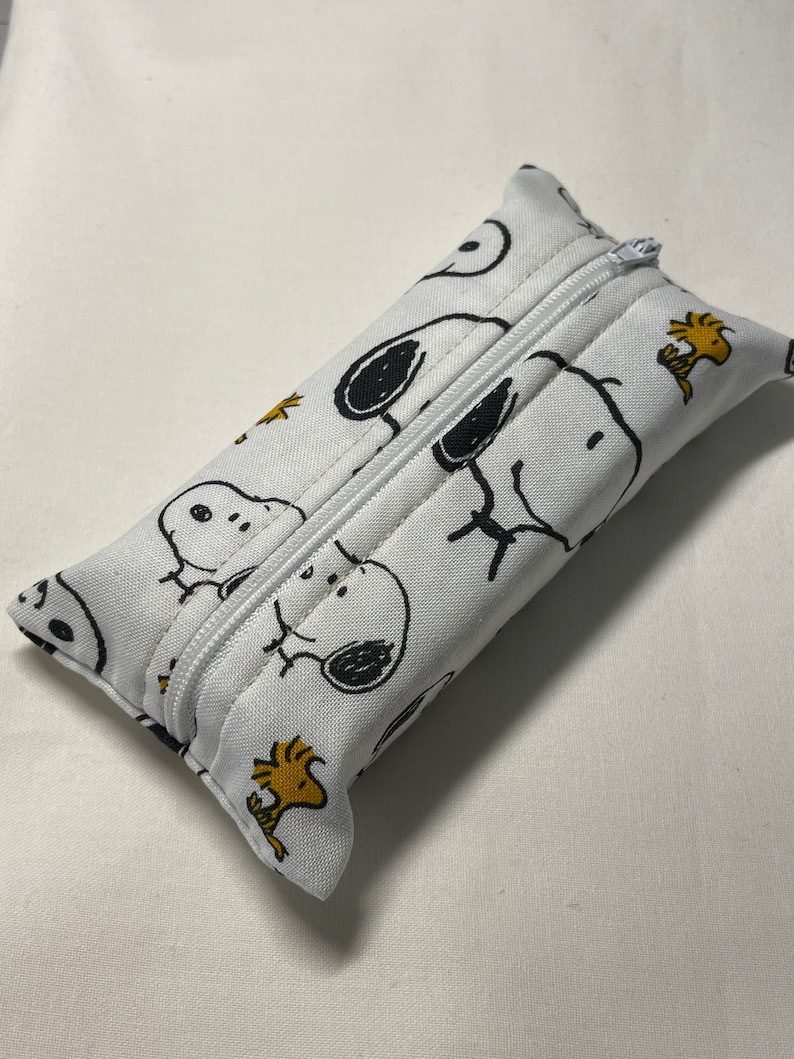 Pu&ograve; includere: Copertura per scatola di fazzoletti in tessuto bianco con chiusura a zip. La copertura presenta un motivo ripetuto di cani di cartoni animati in bianco e nero e uccelli gialli.