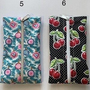 May include: Two rectangular fabric pouches with centre zippers. Pouch 5 features a teal pine branch pattern with pink and blue heart-shaped ornaments. Pouch 6 features a black background with white polka dots and a red cherry and green leaf print.