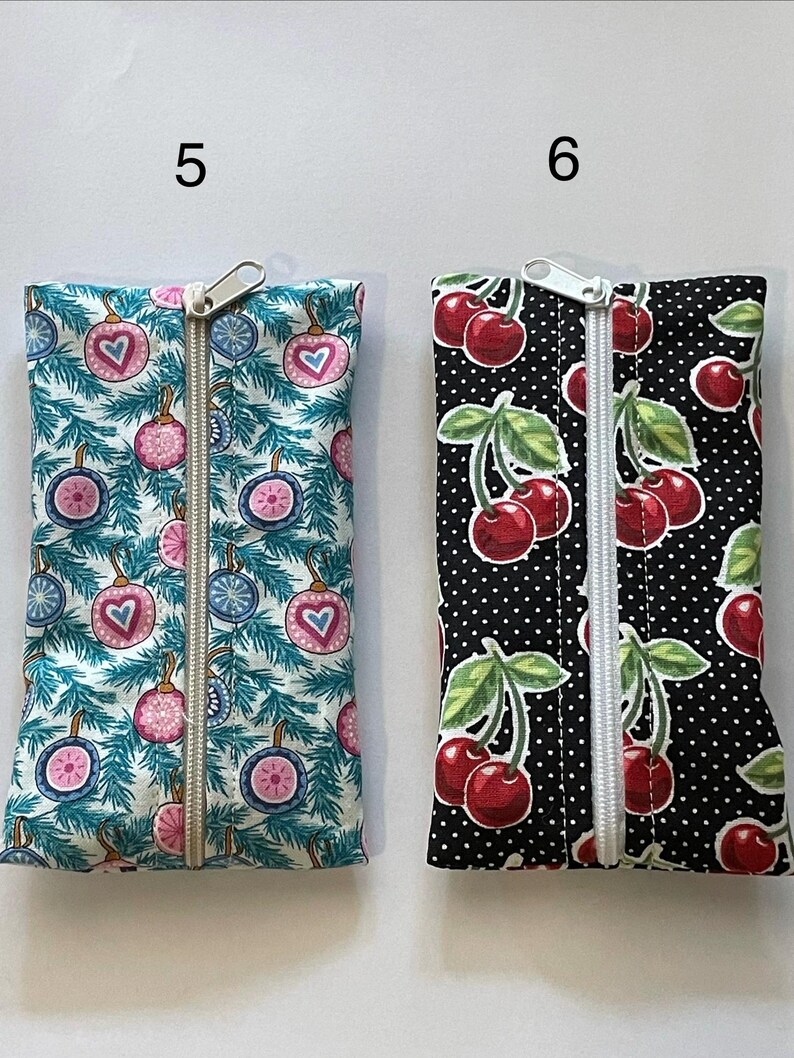 May include: Two rectangular fabric pouches with centre zippers. Pouch 5 features a teal pine branch pattern with pink and blue heart-shaped ornaments. Pouch 6 features a black background with white polka dots and a red cherry and green leaf print.