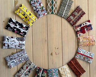 Op de afbeelding: Een collectie van vijftien rechthoekige stoffen etuis met ritssluiting, gerangschikt in een cirkel. Elk etui heeft een uniek patroon, waaronder bloemen-, dieren-, geometrische en feestelijke prints in verschillende kleuren.