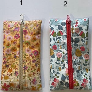 May include: Two rectangular fabric pouches with floral patterns. Pouch 1 features a yellow background with pink, orange, and green flowers and a silver zip. Pouch 2 has a light blue background with blue, pink, and yellow flowers and a red zip.
