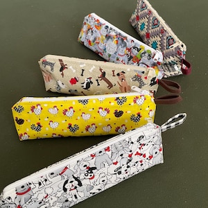May include: Five different patterned zippered pouches. The pouches are made of fabric and have a variety of designs, including dogs, chickens, and geometric patterns. The pouches are all closed and have a zipper closure.