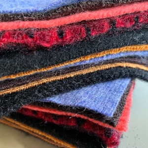 May include: A stack of fabric swatches in various colors, including blue, red, black, brown, and gold. The fabric is soft and textured, with a fuzzy appearance.