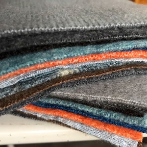 May include: A stack of felt fabric squares in various colors, including gray, brown, blue, and orange. The felt is soft and textured.