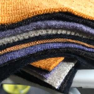 May include: A stack of fabric swatches in various colors, including brown, black, gray, and purple. The swatches are arranged in a staggered pattern, with the top swatch being a bright orange color.