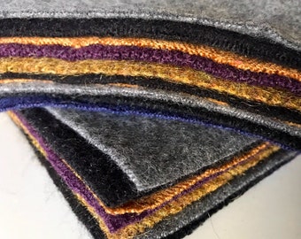 May include: A stack of felt fabric squares in various colors, including gray, black, purple, orange, and gold. The felt is soft and fuzzy, and the edges are neatly cut.