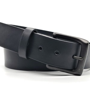 May include: A black leather belt with a rectangular, gunmetal-colored buckle. The belt is curved, showing its flexibility, and has two visible holes. The buckle is a simple, classic design.