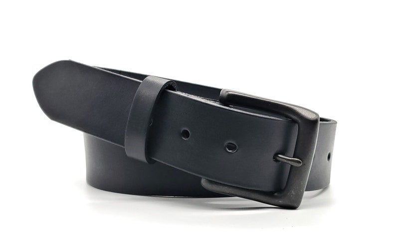 May include: A black leather belt with a rectangular, gunmetal-colored buckle. The belt is curved, showing its flexibility, and has two visible holes. The buckle is a simple, classic design.
