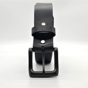 May include: A black leather belt with a dark metal buckle. The belt is rolled up, showing the buckle and the belt loop. The belt is secured with two silver rivets.