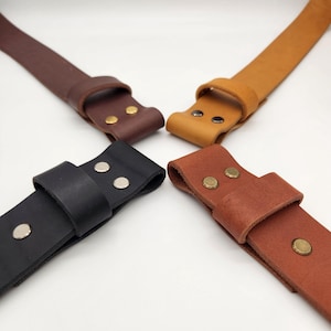 May include: Four leather straps in brown, black, tan, and reddish-brown, each with a loop and secured with rivets. The straps are arranged in a circular pattern against a white background.