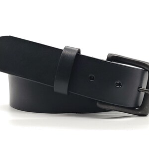 May include: A black leather belt with a rectangular, dark-toned buckle. The belt has a simple design with a single belt loop and a rounded tip. The belt is approximately 1.5 inches wide.