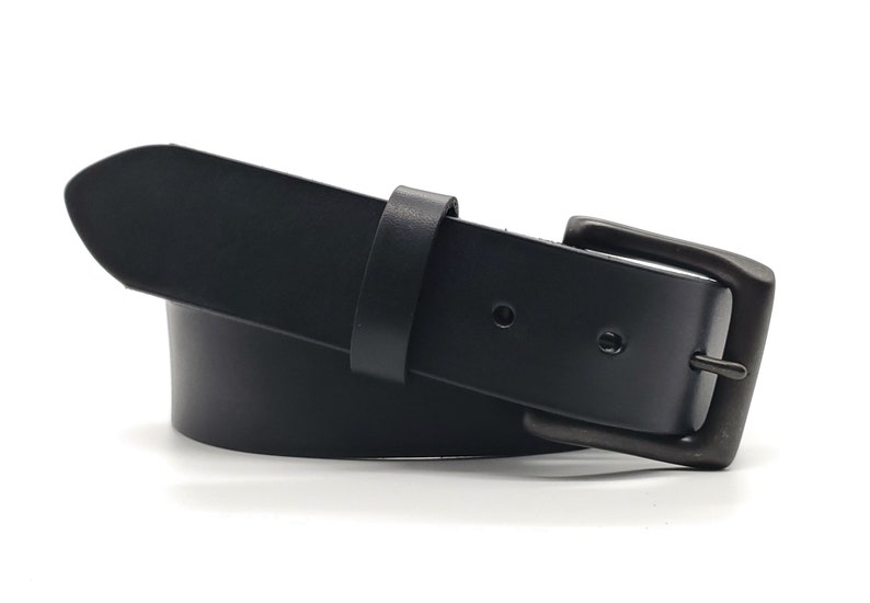 May include: A black leather belt with a rectangular, dark-toned buckle. The belt has a simple design with a single belt loop and a rounded tip. The belt is approximately 1.5 inches wide.