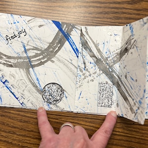 May include: A white paper journal with blue and gray ink splatter designs. The text "find joy" is written on the front cover.