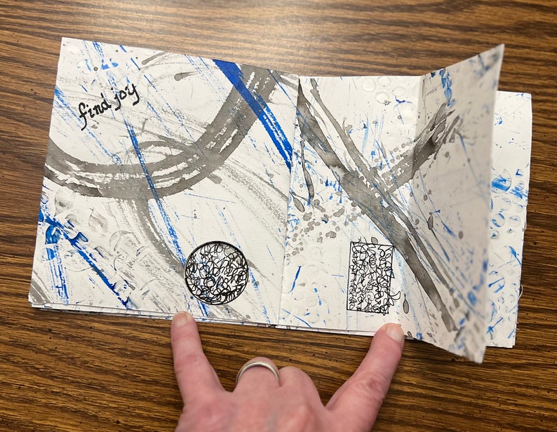 May include: A white paper journal with blue and gray ink splatter designs. The text "find joy" is written on the front cover.