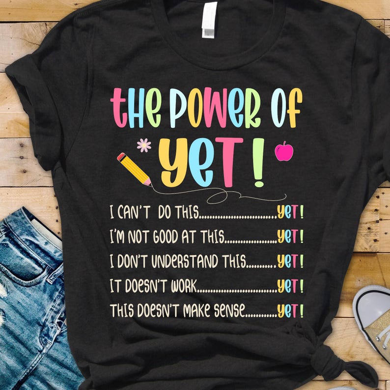 May include: Black t-shirt with the text "the Power of *yet!" in colorful letters. Below the text are the phrases "I CAN'T DO THIS...yet!", "I'M NOT GOOD AT THIS...yet!", "I DON'T UNDERSTAND THIS...yet!", "IT DOESN'T WORK...yet!", and "THIS DOESN'T MAKE SENSE...yet!"