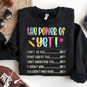 May include: Black sweatshirt with the text "the POWER of YET!" in colorful letters. The design includes a pencil, an apple, and the phrases "I CAN'T DO THIS...yet!" and "I'M NOT GOOD AT THIS...yet!"