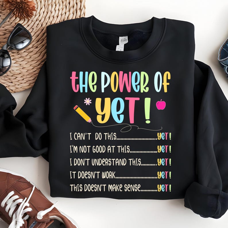 May include: Black sweatshirt with the text "the POWER of YET!" in colorful letters. The design includes a pencil, an apple, and the phrases "I CAN'T DO THIS...yet!" and "I'M NOT GOOD AT THIS...yet!"