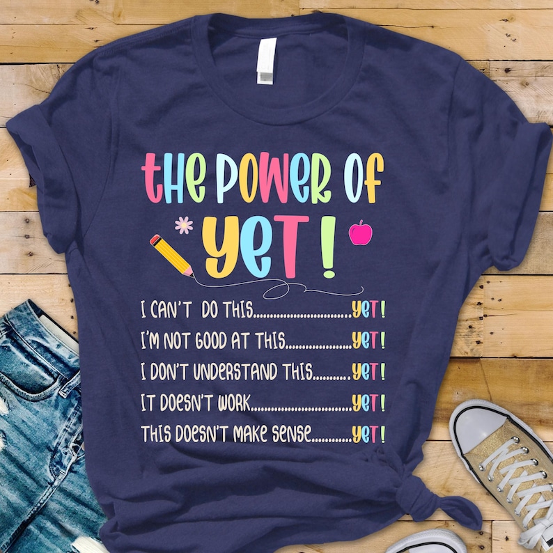 May include: Navy blue t-shirt with the text "The Power of Yet!" in colorful letters. The shirt includes phrases like "I can't do this...yet!" and "I'm not good at this...yet!" with a pencil and apple graphic.