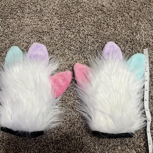 May include: Pair of white faux fur gloves with pastel-colored fingertips. The fingertips are light blue, lavender, and pink. The gloves have black cuffs and are approximately 10 inches long.