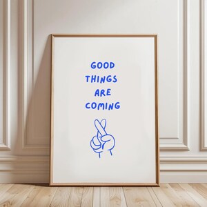 May include: A white framed poster with blue text that reads "GOOD THINGS ARE COMING" and a blue illustration of a hand with crossed fingers.