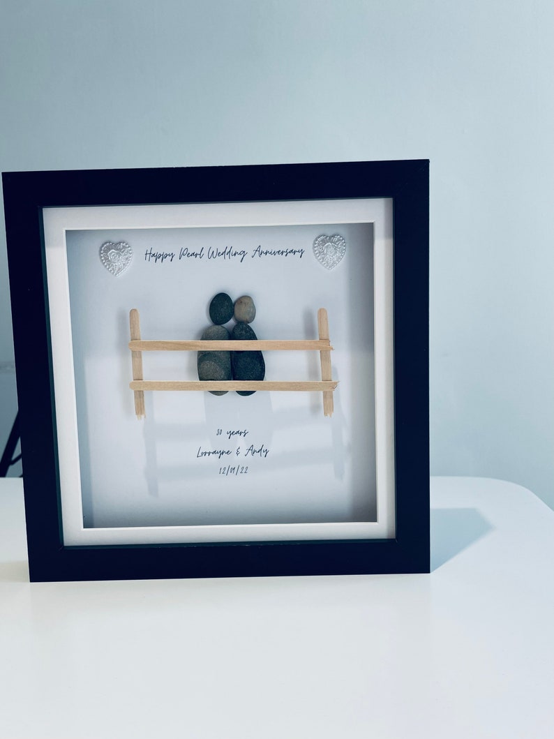May include: A framed pebble art piece depicting a couple sitting on a bench. The art is titled "Happy Pearl Wedding Anniversary" and includes the text "30 years Lorraine & Andy 12/10/22".