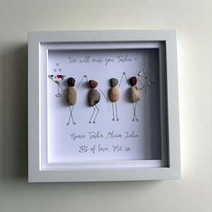 May include: A white framed picture with a hand-drawn image of four stick figures holding hands. The figures are made of small, colorful stones. The text "We will miss you Tasha" and "Grace Tasha Alicia Julie" is written in black ink. The text "Lots of love. M2 xx" is also written in black ink.