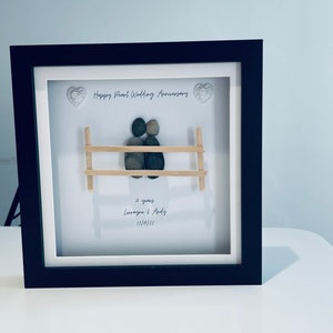 May include: A framed pebble art piece depicting a couple sitting on a bench. The art is titled "Happy Pearl Wedding Anniversary" and includes the text "30 years Lorraine & Andy 12/10/22".