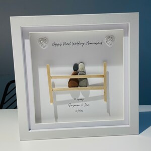 May include: A white framed picture with a pebble art design of a couple sitting on a bench. The text reads "Happy Pearl Wedding Anniversary 30 years Suzanne & Ian 24/1/1992".