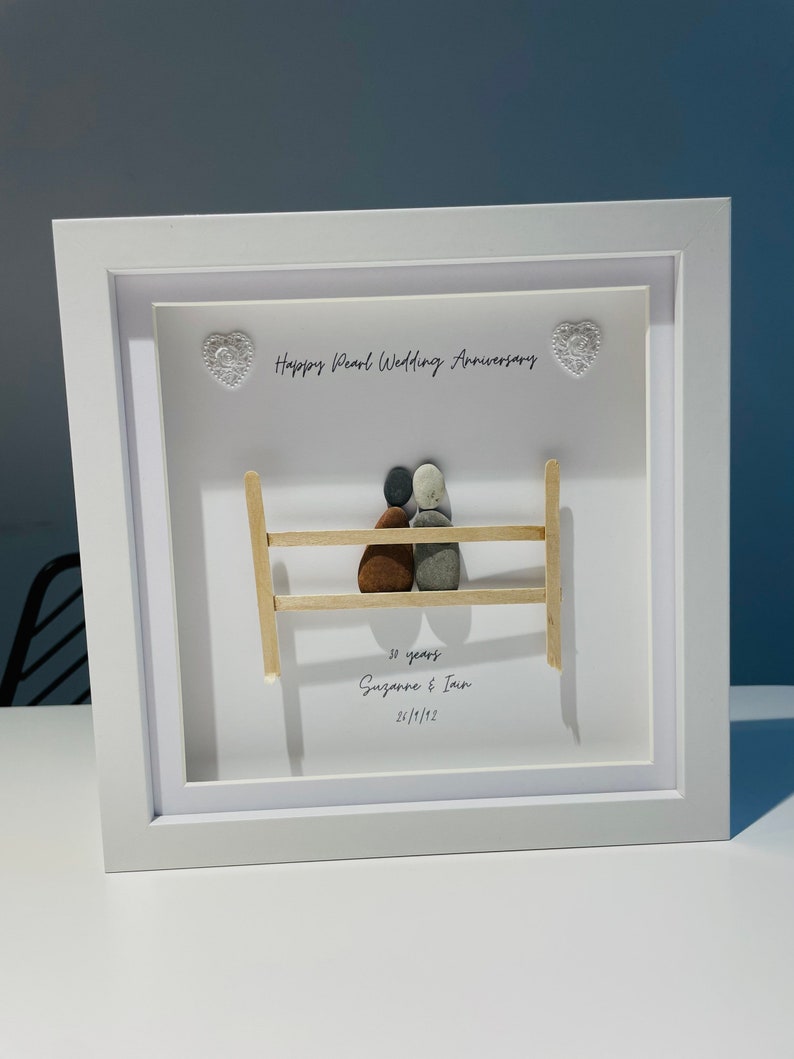 May include: A white framed picture with a pebble art design of a couple sitting on a bench. The text reads "Happy Pearl Wedding Anniversary 30 years Suzanne & Ian 24/1/1992".