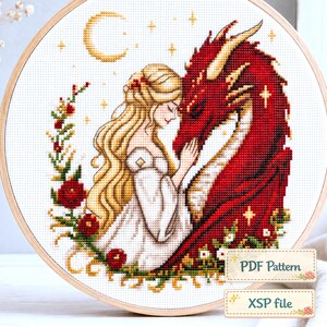 Pode incluir: Um bordado em ponto cruz num bastidor de madeira redondo com uma pessoa loira de vestido branco a tocar num grande dragão vermelho. O design inclui uma lua crescente amarela, estrelas e rosas vermelhas. Texto: PDF Pattern e XSP file.