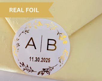 May include: A white round sticker with gold foil lettering and a floral design. The sticker says "A|B 11.30.2025".