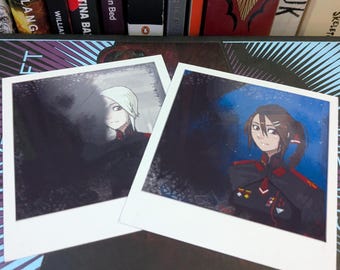 May include: Two square photographic prints featuring anime-style character illustrations. The left print shows a character with white hair in a dark uniform. The right print depicts a character with brown hair in a dark uniform with red accents.