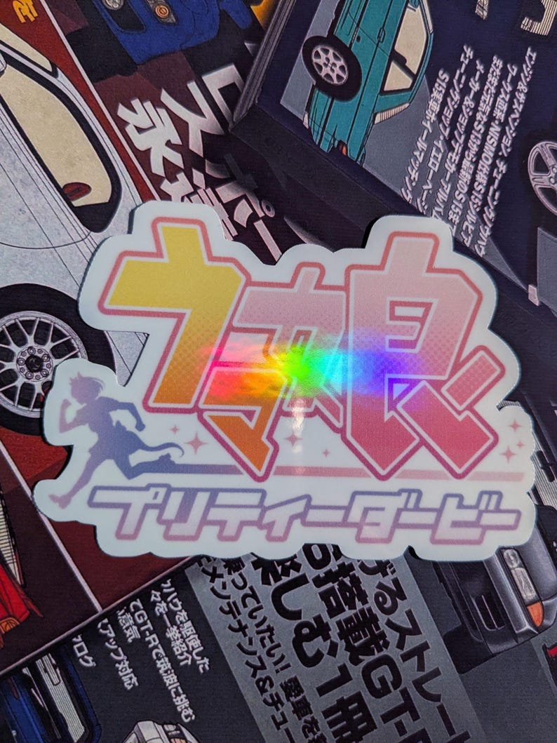 May include: A holographic sticker with Japanese text and a running figure silhouette. The sticker has a pink and purple gradient with a rainbow effect. The text includes the words "Pretty Derby".