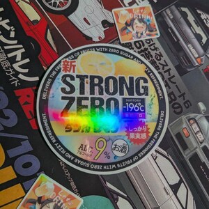 May include: A collection of stickers and decals featuring Japanese text and anime-style illustrations. The central sticker is a holographic circle with the text "STRONG ZERO" and "-196°C". Other stickers include images of cars and anime characters.