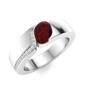 Pode incluir: Um anel de prata com uma gema vermelha e uma fileira de gemas transparentes menores de um lado.