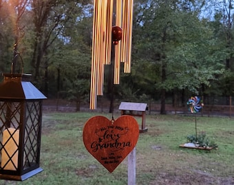 May include: A wooden heart-shaped wind chime with the text "All you need is love Grandma" and a decorative metal wind chime with silver tubes hanging from a wooden frame.