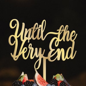 May include: Gold cake topper with the words "Until the Very End" in a cursive font.