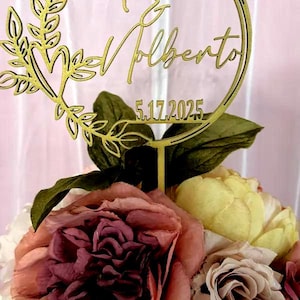Pu&ograve; includere: Un cake topper dorato con i nomi "& Valberto" e la data "5.17.2025" &egrave; posto su una composizione floreale. Il topper &egrave; circondato da una ghirlanda decorativa. I fiori sono di varie tonalit&agrave; di rosa, giallo e crema.