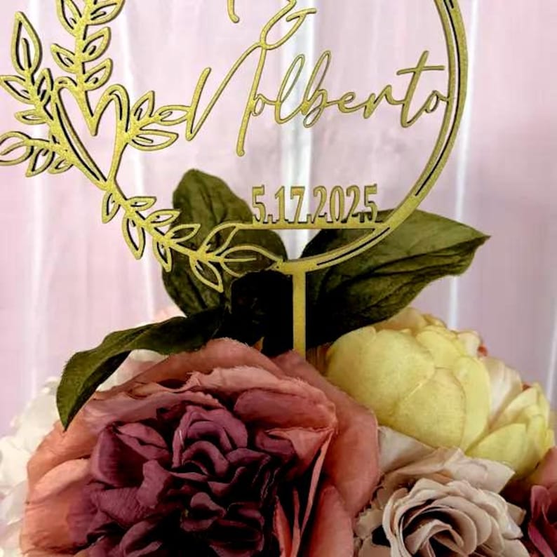 Pu&ograve; includere: Un cake topper dorato con i nomi "& Valberto" e la data "5.17.2025" &egrave; posto su una composizione floreale. Il topper &egrave; circondato da una ghirlanda decorativa. I fiori sono di varie tonalit&agrave; di rosa, giallo e crema.